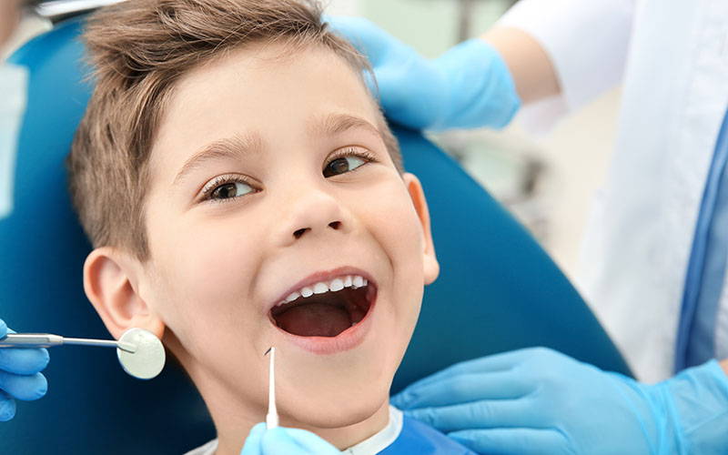 Smiling child at the dentist with open mouth and dental tools.